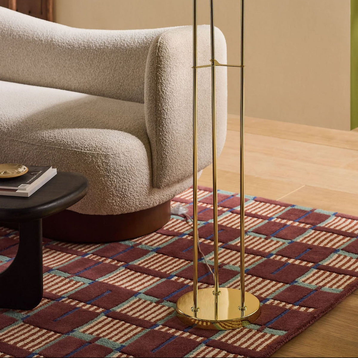 Gold metal floor lamp with three vertical poles on a patterned rug next to a cream sofa