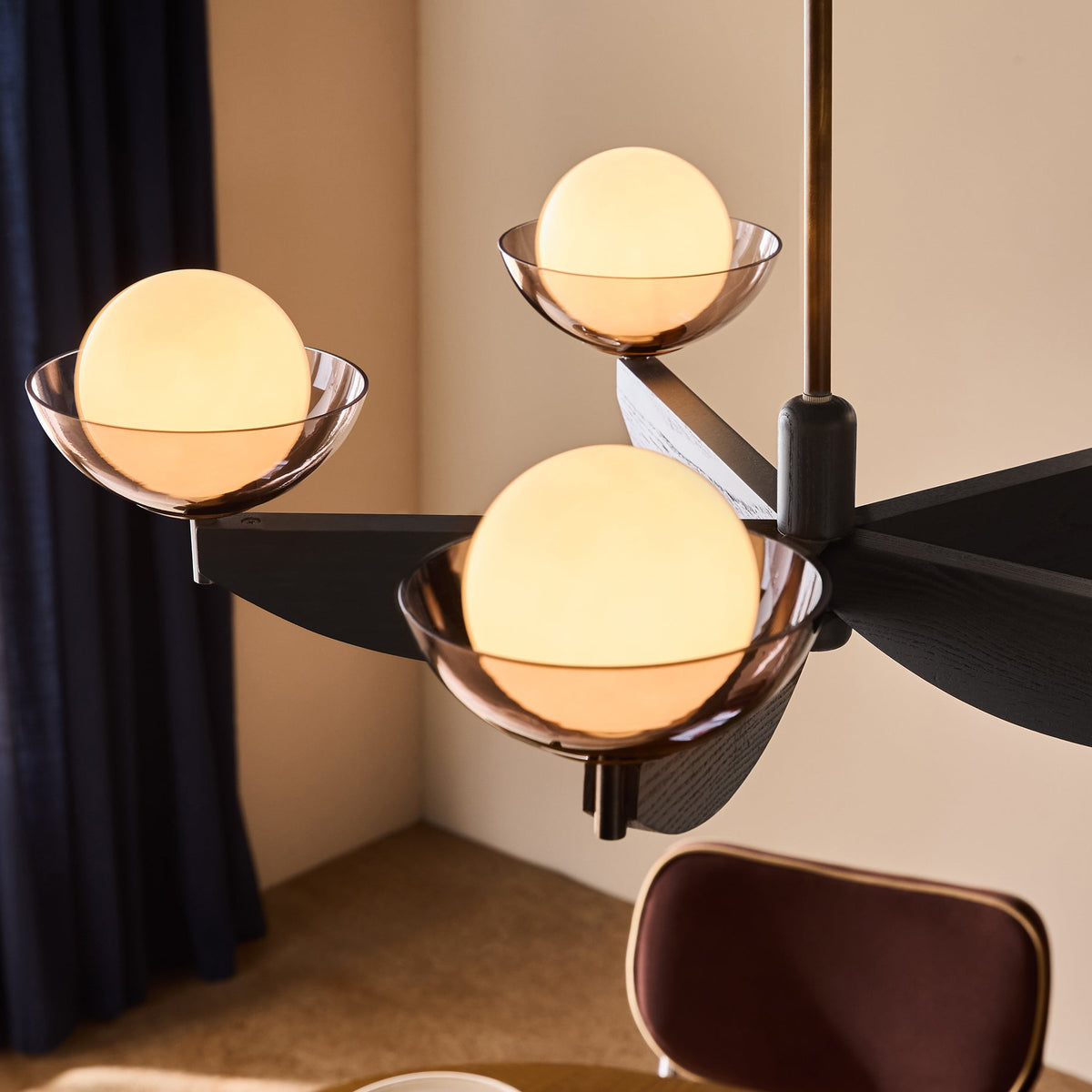 Modern chandelier with three glowing spherical bulbs in tinted glass bowls on a black wooden frame
