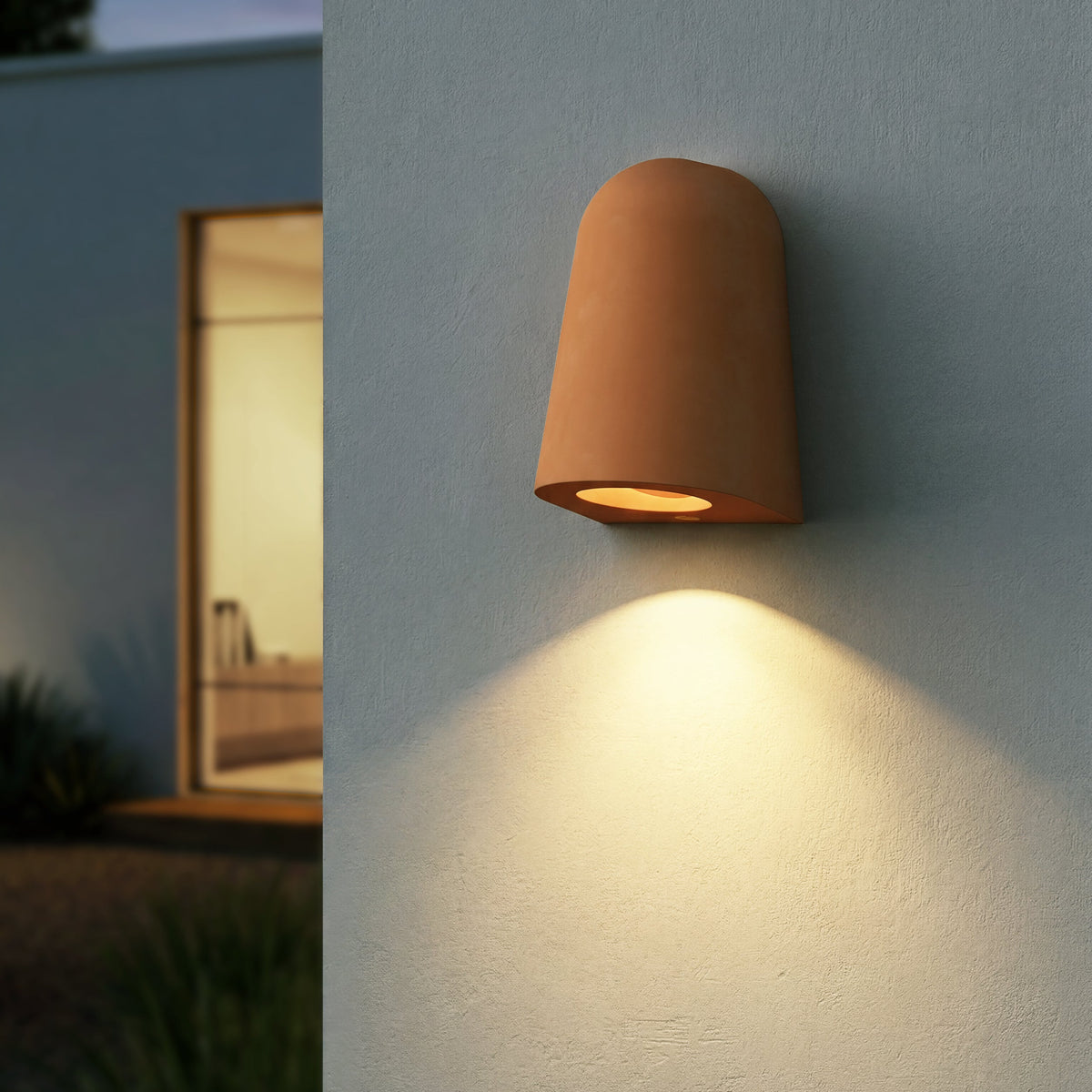 Terracotta wall light illuminating a textured wall at dusk