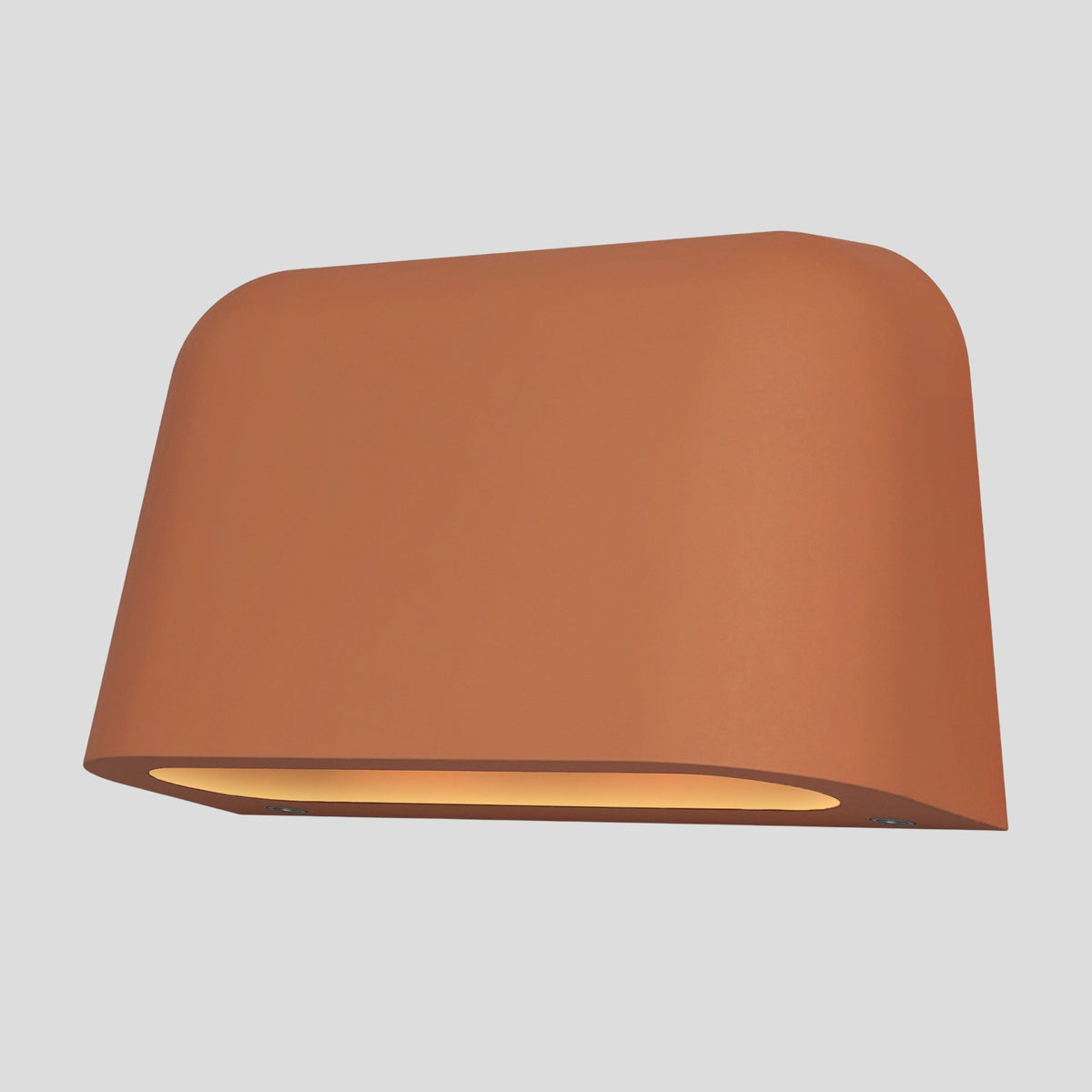 Terracotta colored wall light with a curved top and bottom, emitting a warm glow from its underside