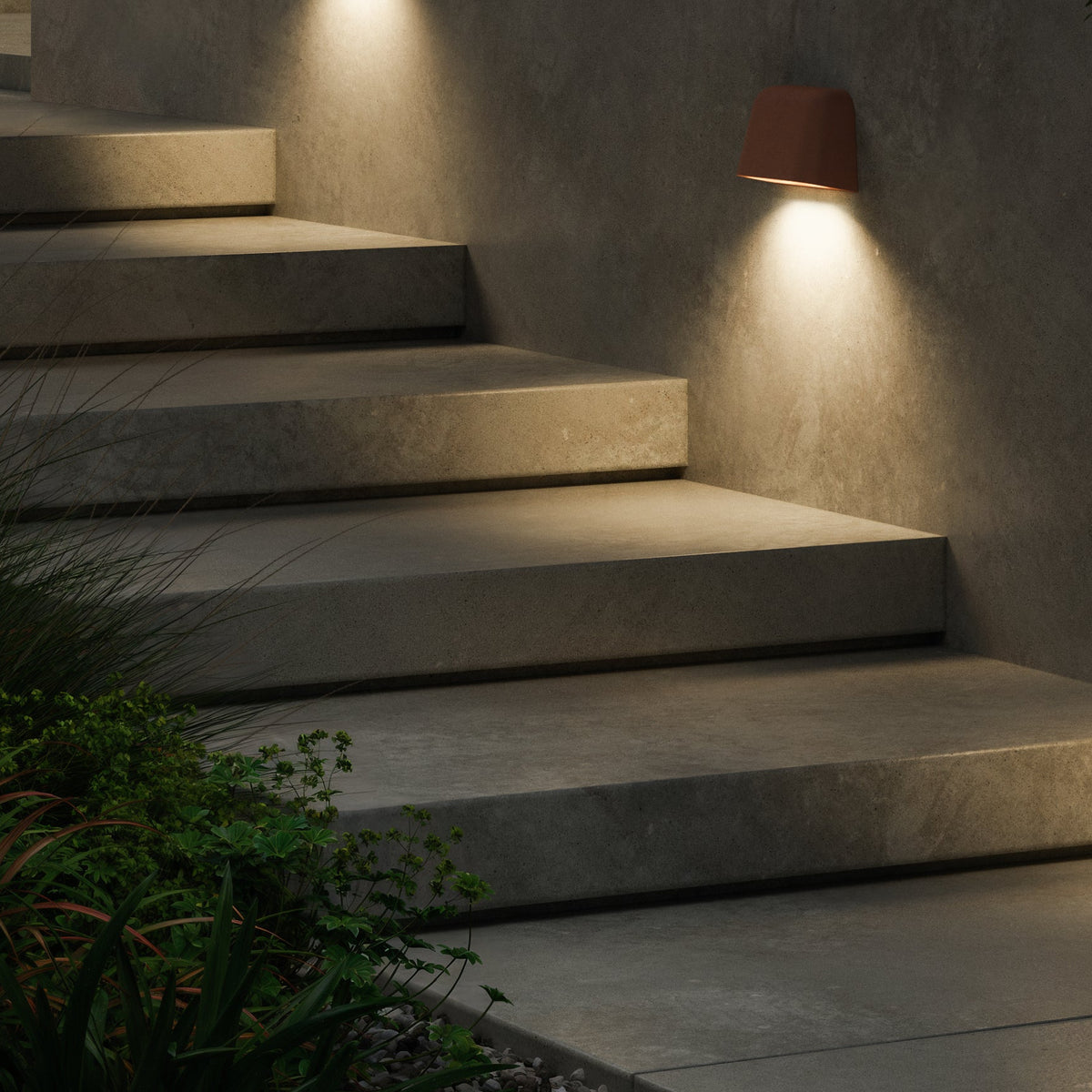 Concrete steps with a wall-mounted light fixture and green plants at the base
