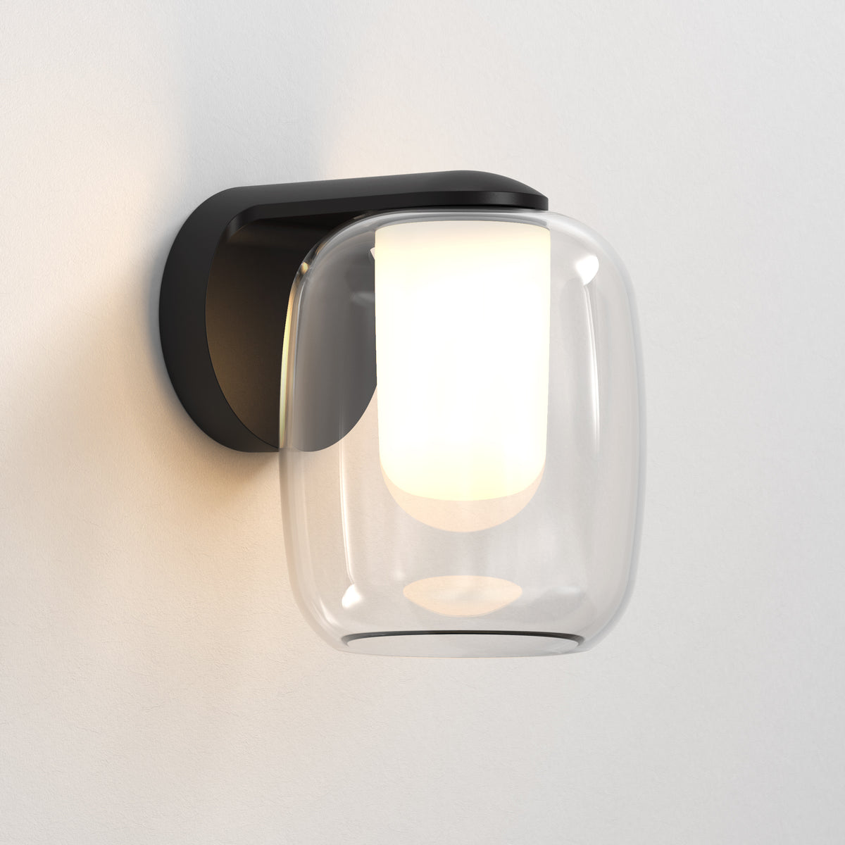 Black wall sconce with a clear glass shade and an illuminated white cylindrical bulb