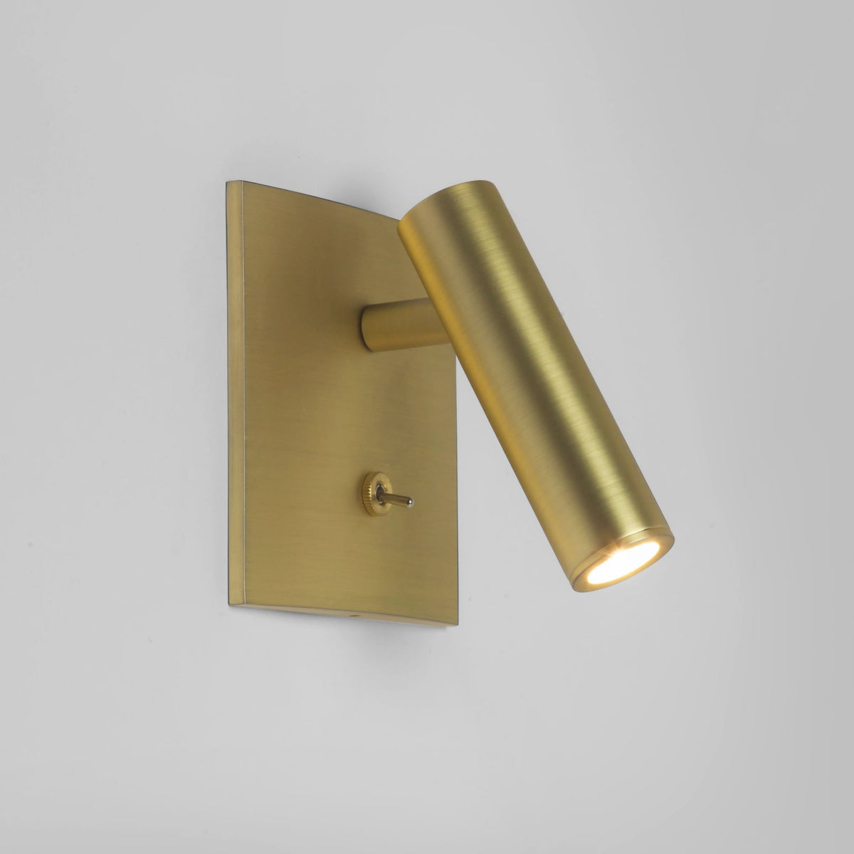 Brass wall light with a square base and a cylindrical adjustable head, featuring a small toggle switch