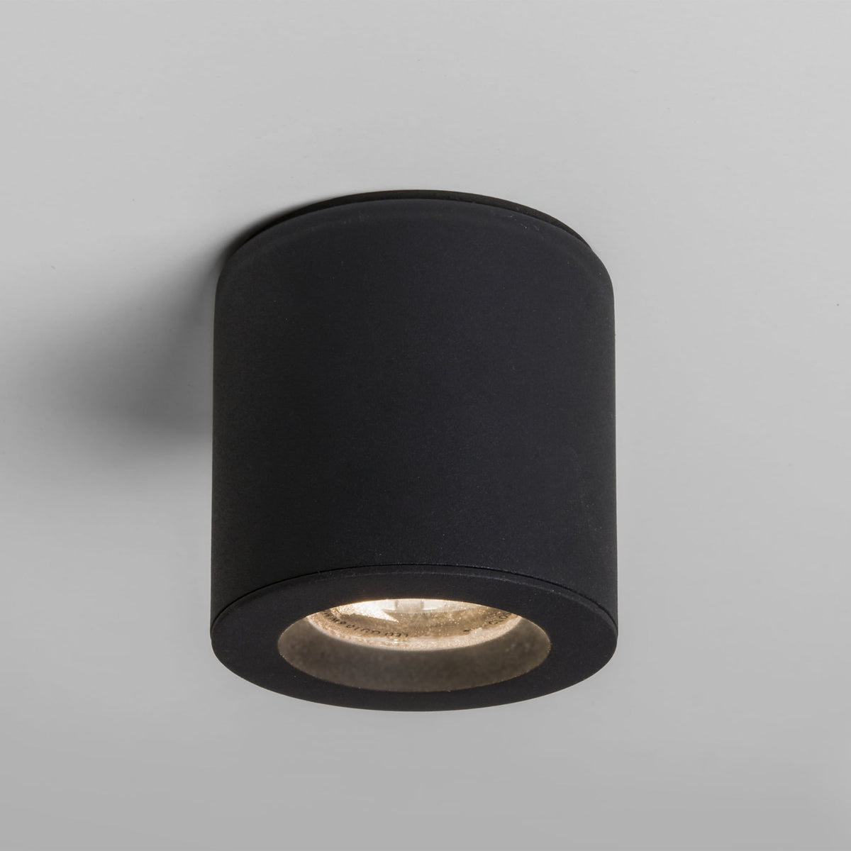 Black cylindrical ceiling light with a warm glowing bulb