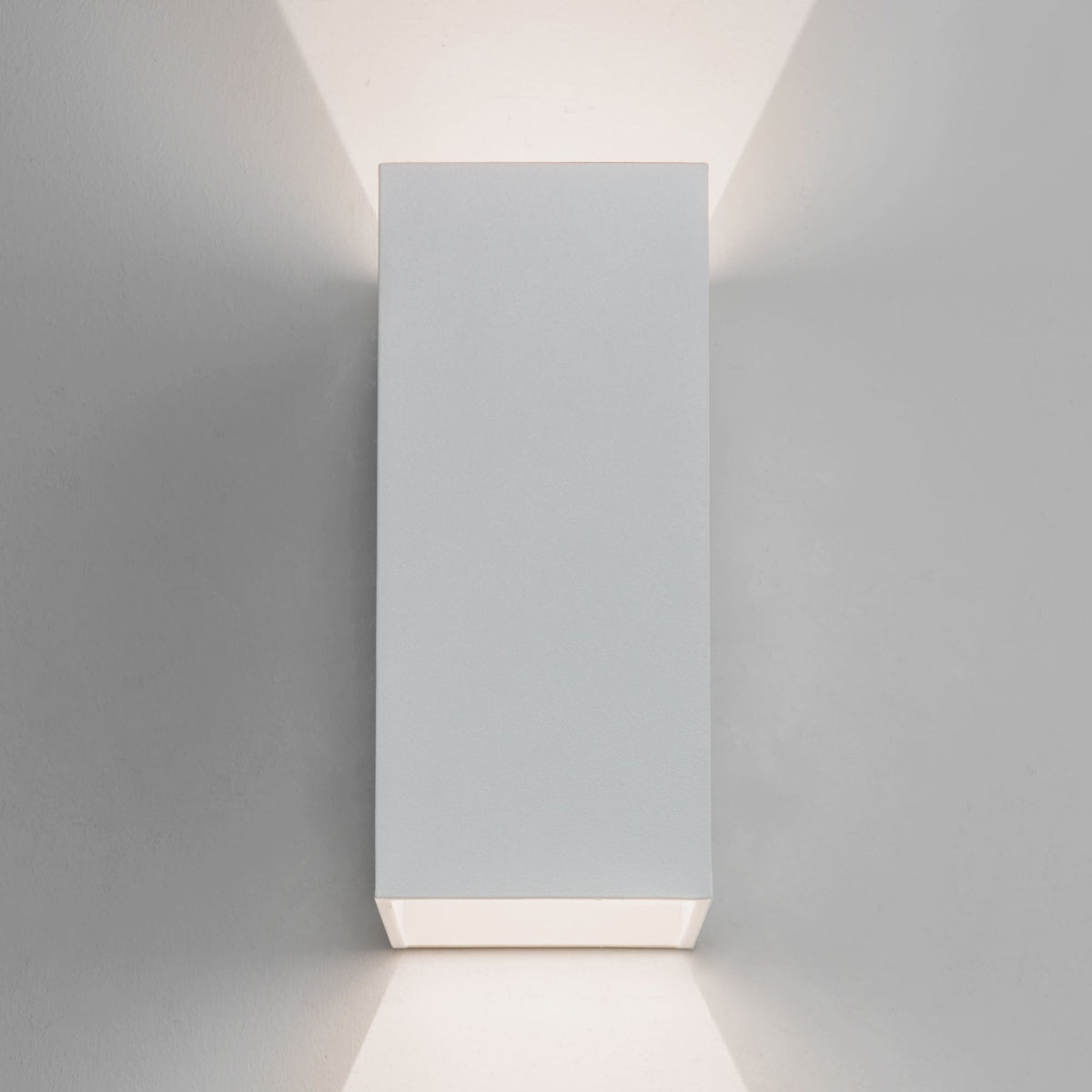 Rectangular white wall light with light shining upwards and downwards on a grey wall