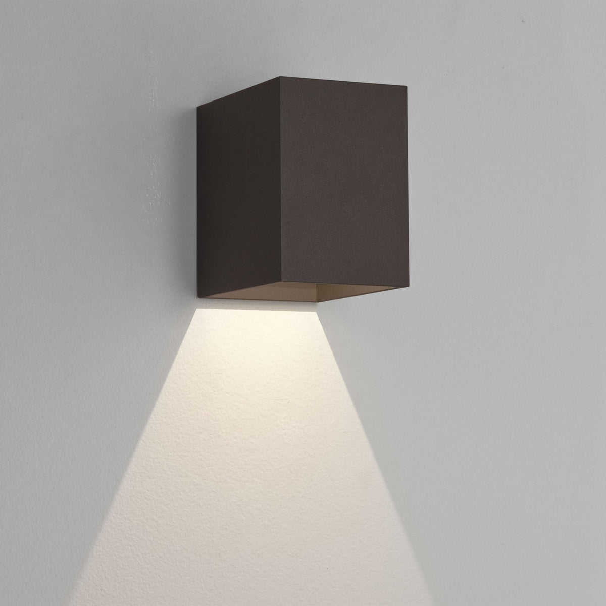 Dark brown cube-shaped wall light fixture casting a downward beam of light on a white wall