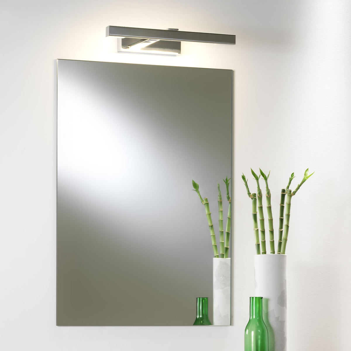 Rectangular mirror with a horizontal light fixture above it, and two vases with bamboo stalks to the right