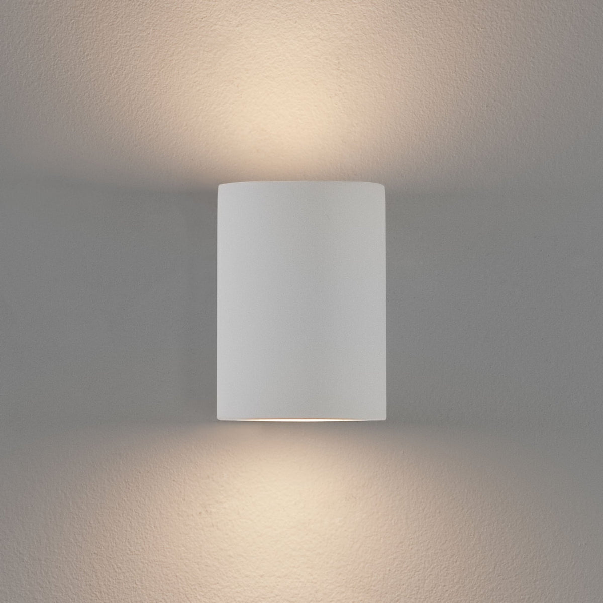 White rectangular wall light fixture with rounded edges, casting warm light upwards and downwards on a textured wall