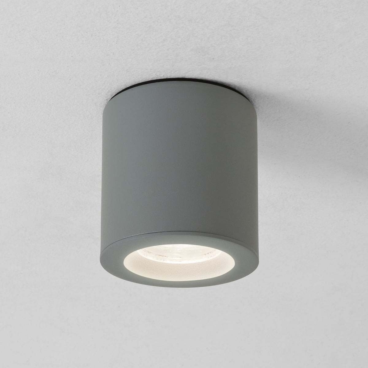 Grey cylindrical ceiling light fixture with a bright, illuminated bulb