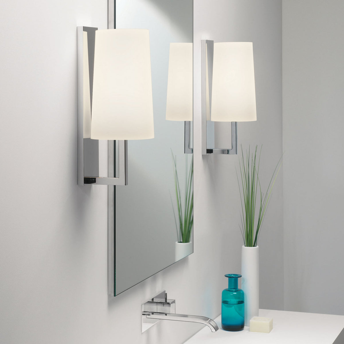 Two wall-mounted sconces with rectangular shades flank a mirror above a sink with a chrome faucet