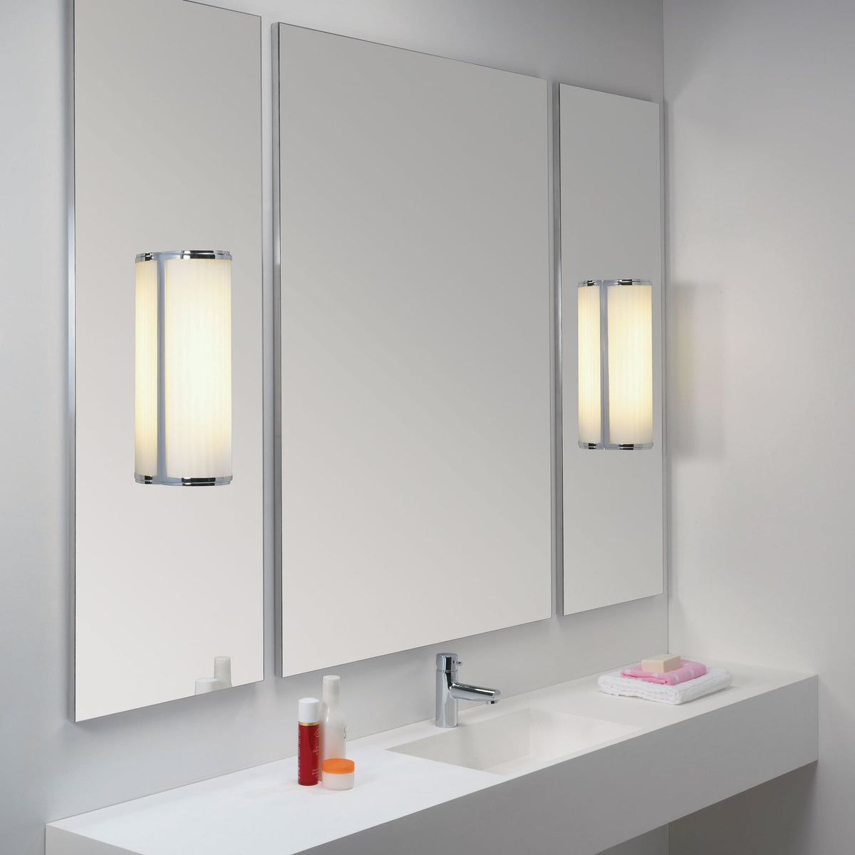 Bathroom vanity with three mirrors, two wall sconces, a sink, and toiletries