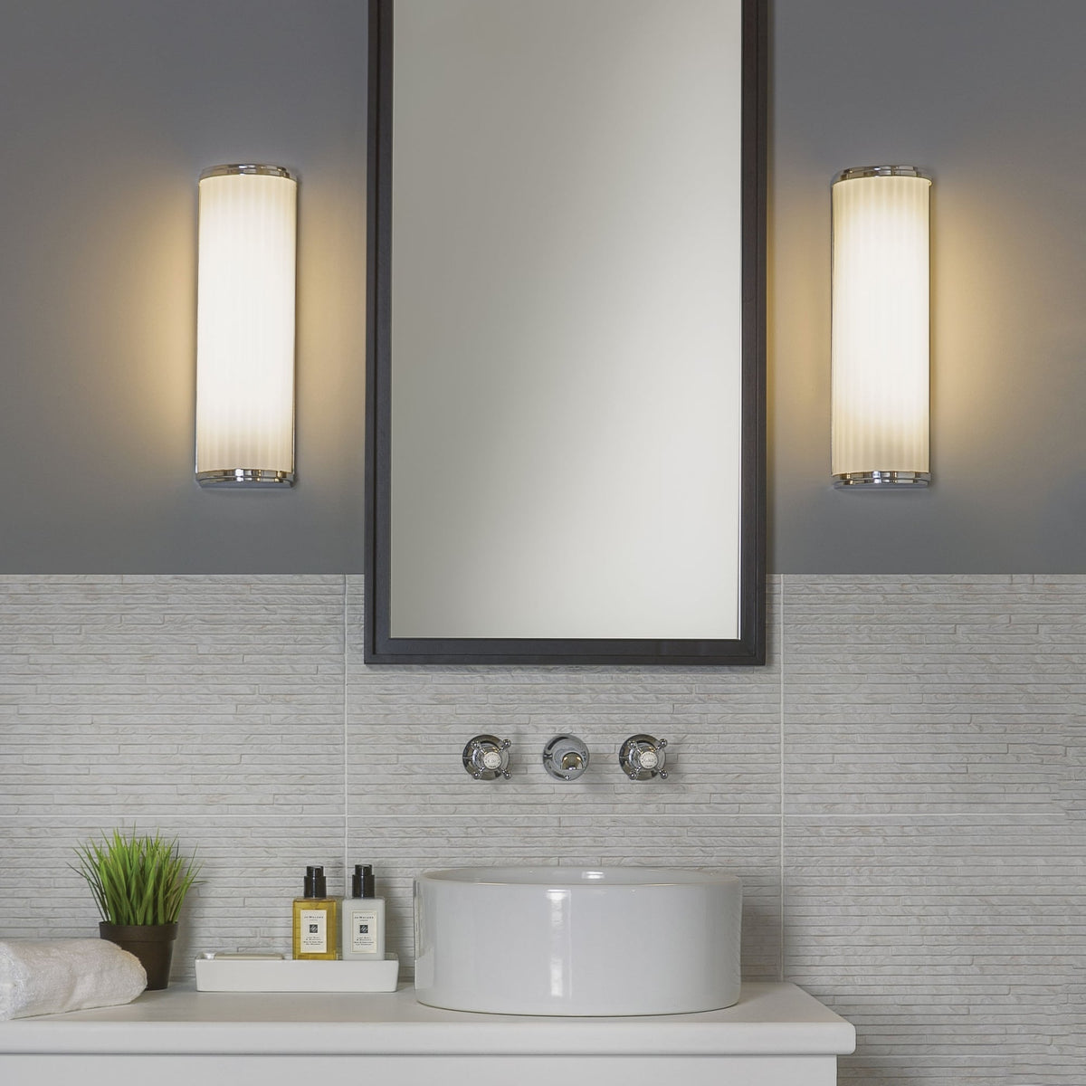 Bathroom with white vessel sink, wall-mounted faucet, rectangular mirror, and two vertical wall sconces
