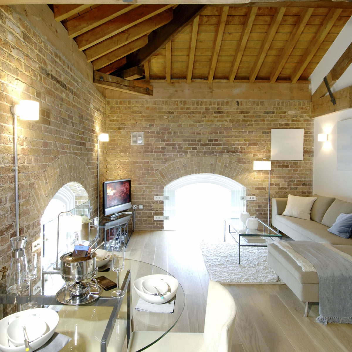 Living room with exposed brick walls, light wood floor, and a high vaulted ceiling with wooden beams