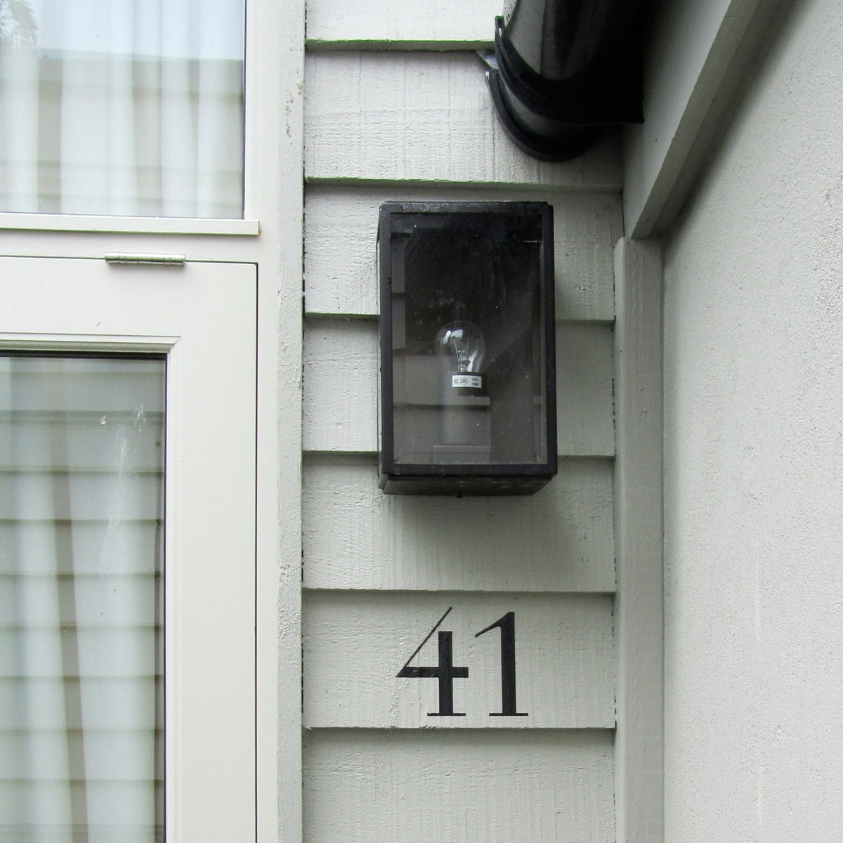 Black house numbers 41 on light gray siding next to a dark outdoor light.