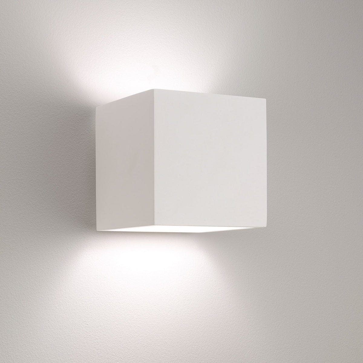 White cube-shaped wall light fixture casting light upwards and downwards on a textured white wall
