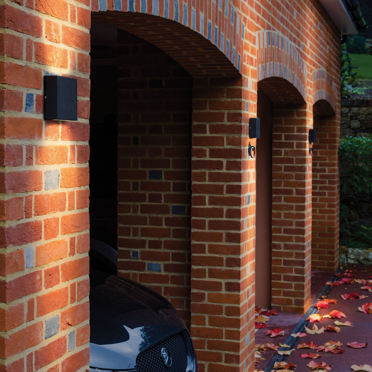 Black outdoor wall light on a brick garage wall with a car parked inside