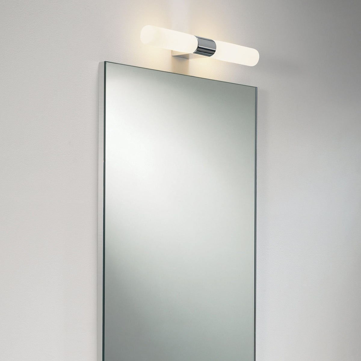 Chrome and white cylindrical light fixture above a rectangular mirror