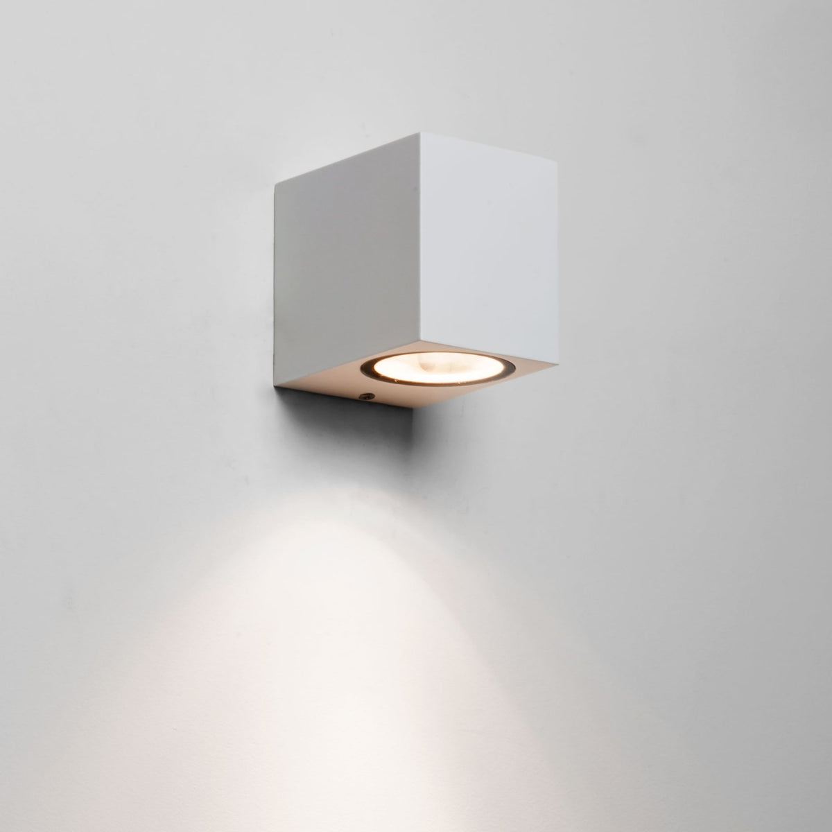 White square wall light with a circular bulb casting a warm glow downwards on a white wall