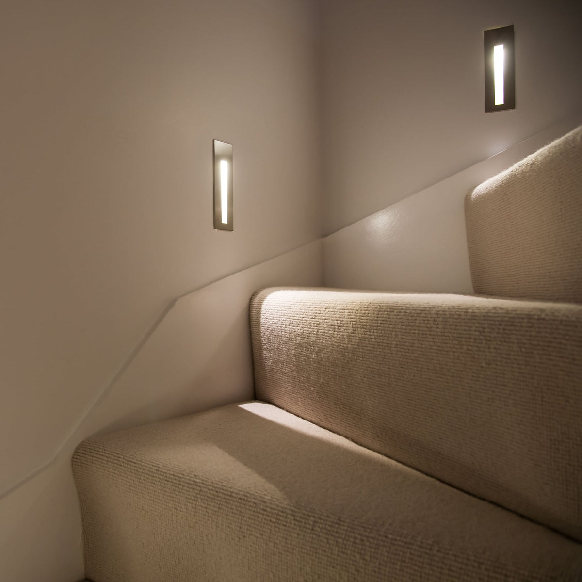 Staircase with beige carpet and three rectangular wall lights illuminating the steps
