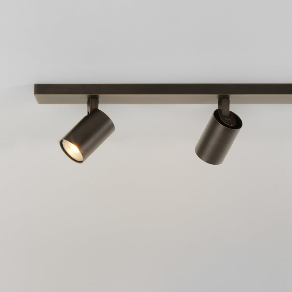 Two dark bronze track lights on a white ceiling, one illuminated