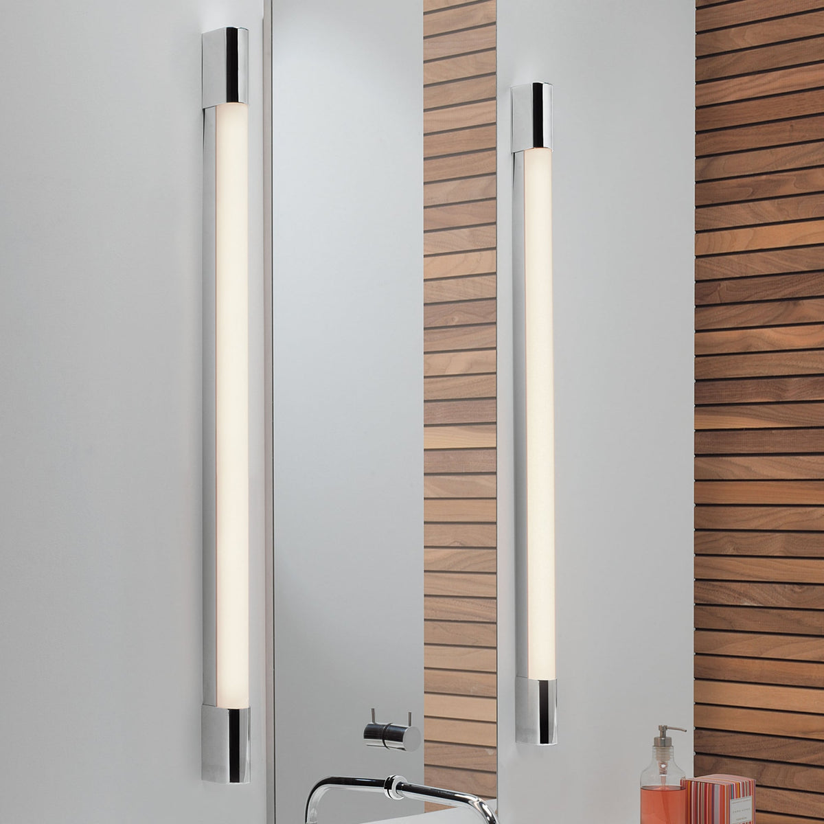 Two vertical chrome and frosted glass light fixtures flank a mirror over a sink