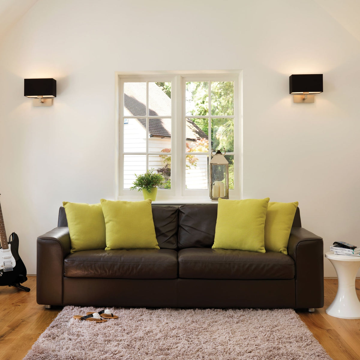 Living room with a brown sofa, lime green pillows, and two wall sconces.