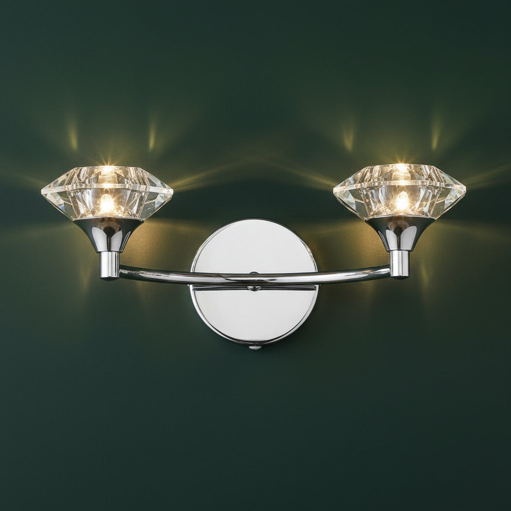 Chrome wall sconce with two diamond-shaped crystal shades, illuminated on a white background.