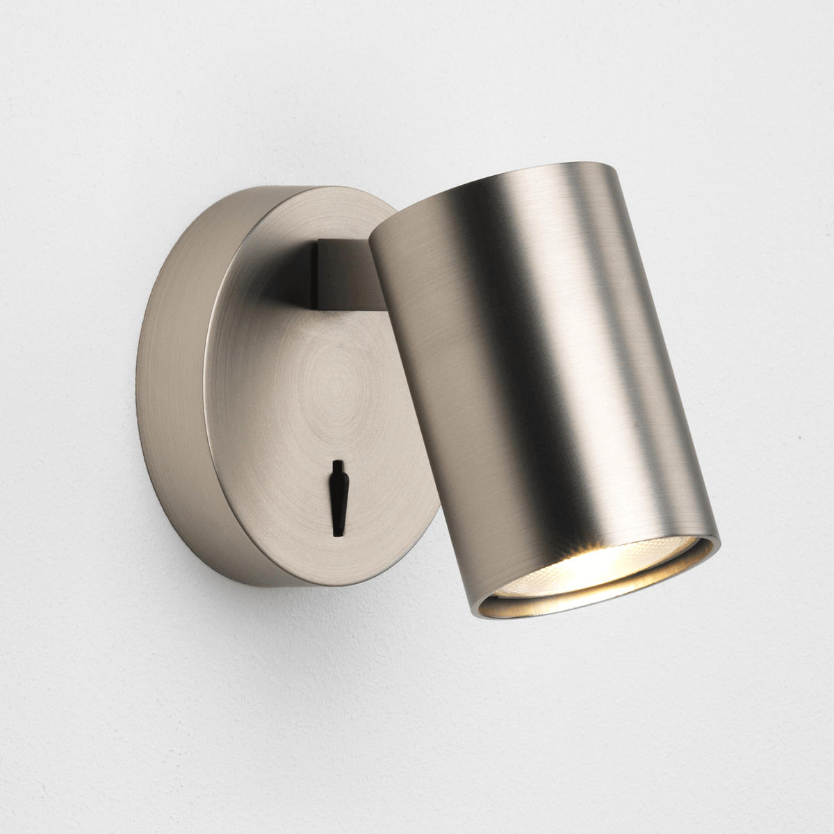 A close-up shot of a switched-on, brushed steel wall light with a cylindrical head.