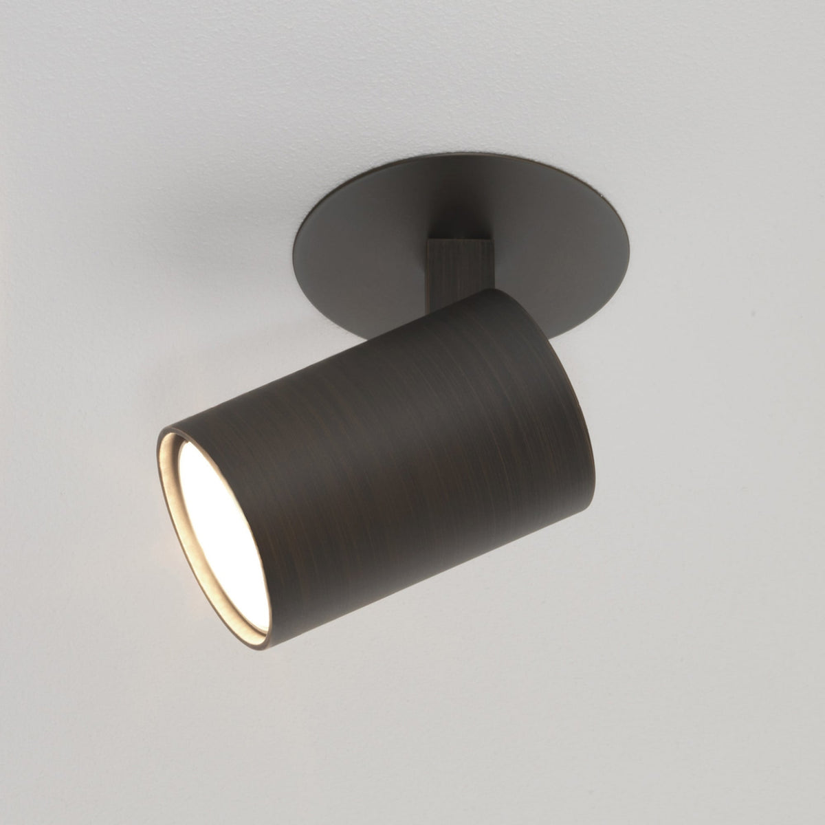 Bronze ceiling spotlight with a cylindrical head and a round base, angled downwards with light emitting