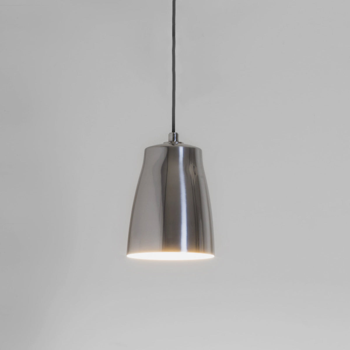 Polished chrome pendant light with a black cord against a light gray wall