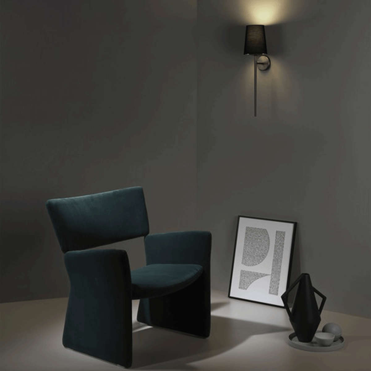 Dark teal armchair in a corner with a wall sconce, framed art, and decorative vase on a tray