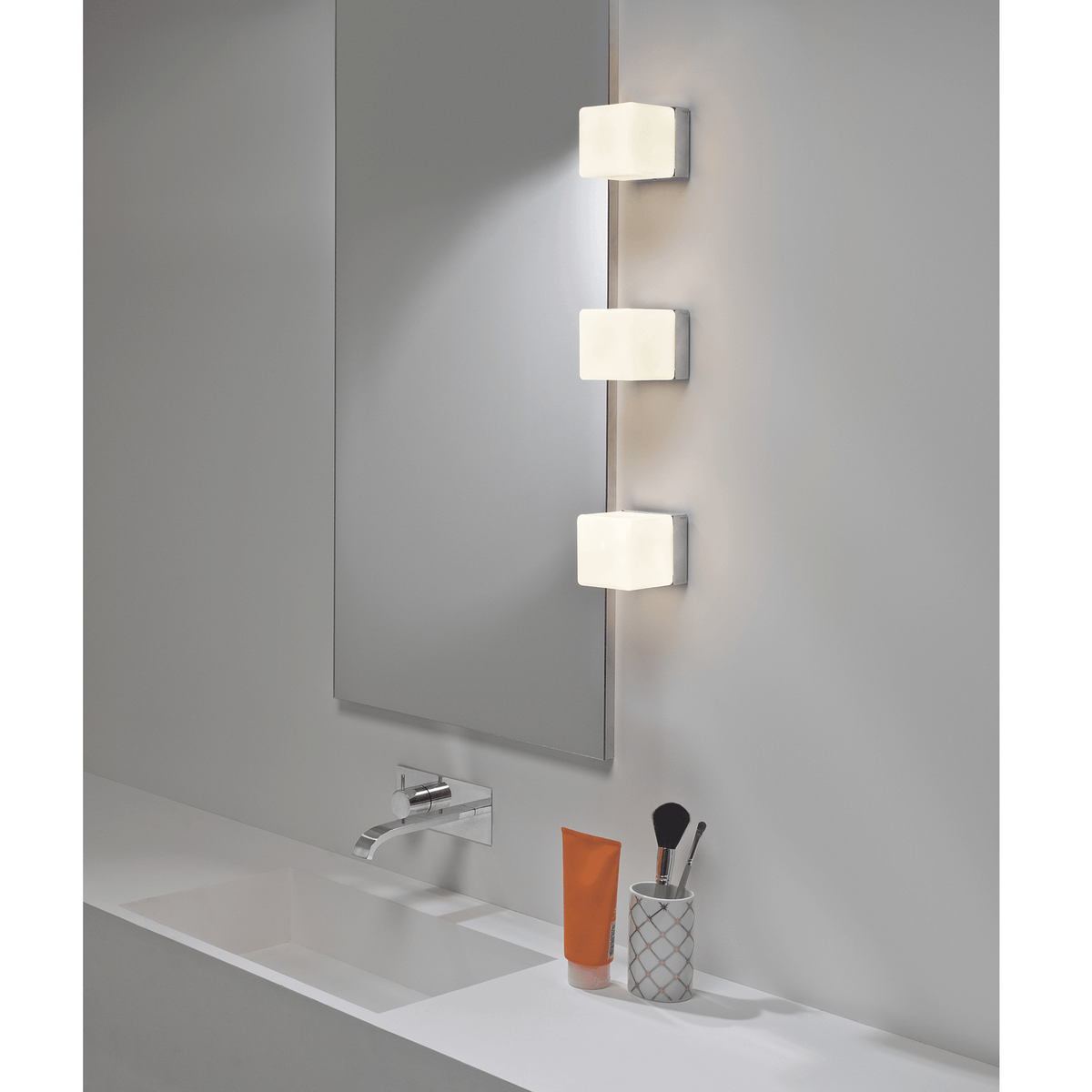 Three rectangular vanity lights mounted vertically beside a mirror over a bathroom sink.
