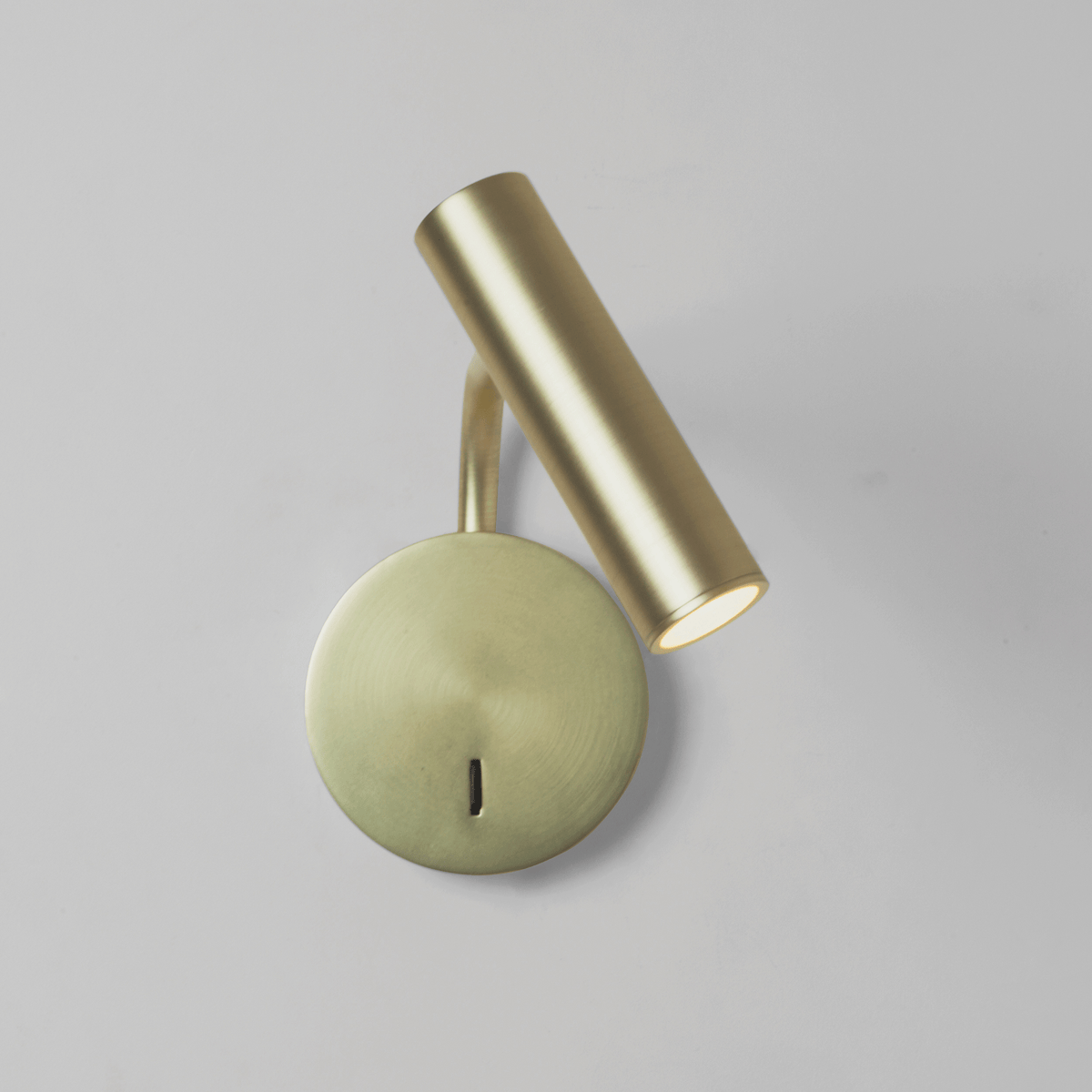 Brass wall lamp with a circular base and a cylindrical light pointing downwards