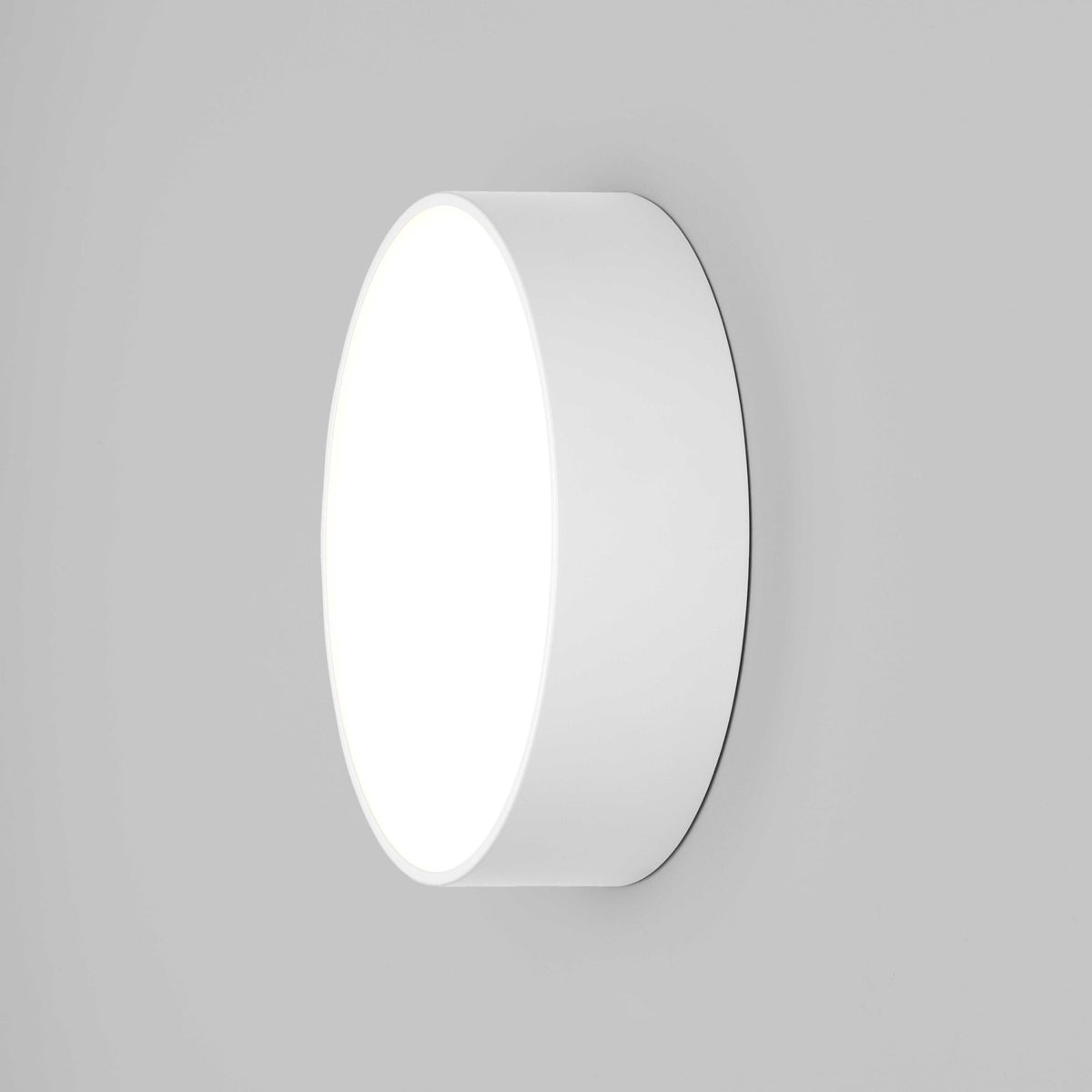 A white circular light fixture is mounted on a grey wall, emitting a bright glow.