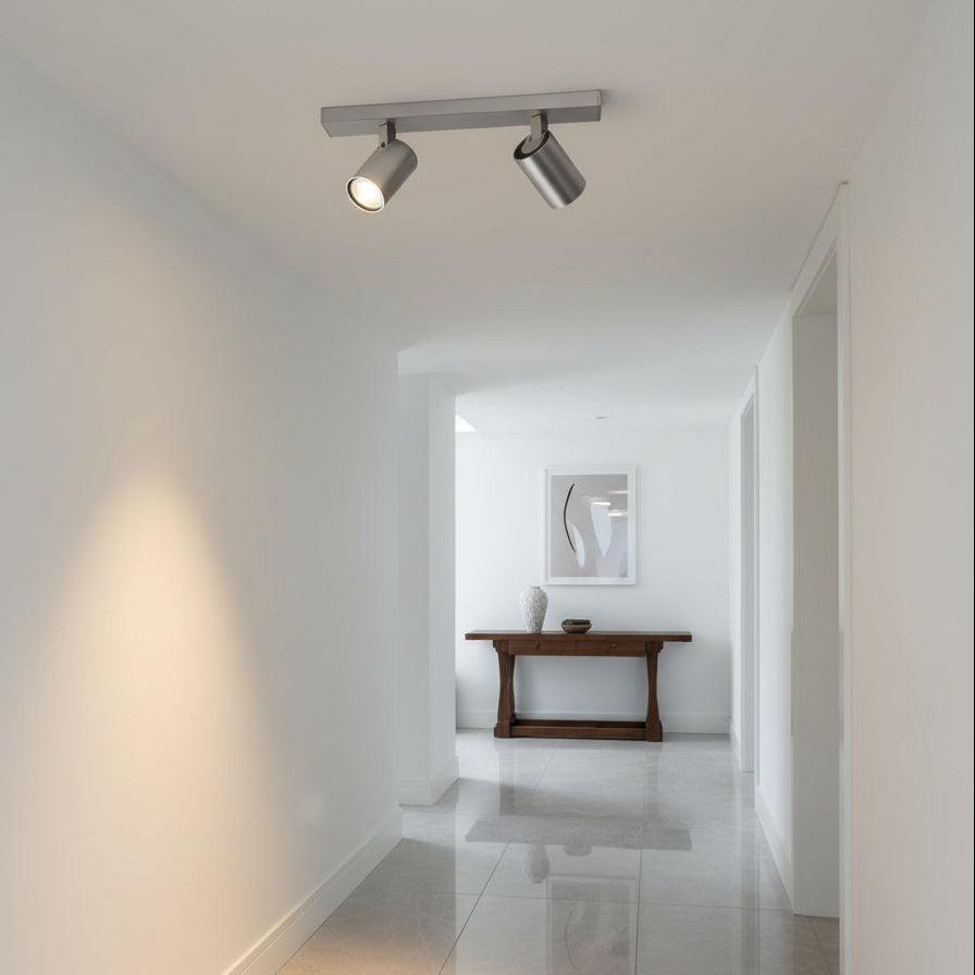 Two brushed steel ceiling spotlights illuminating a white hallway with a wooden console table