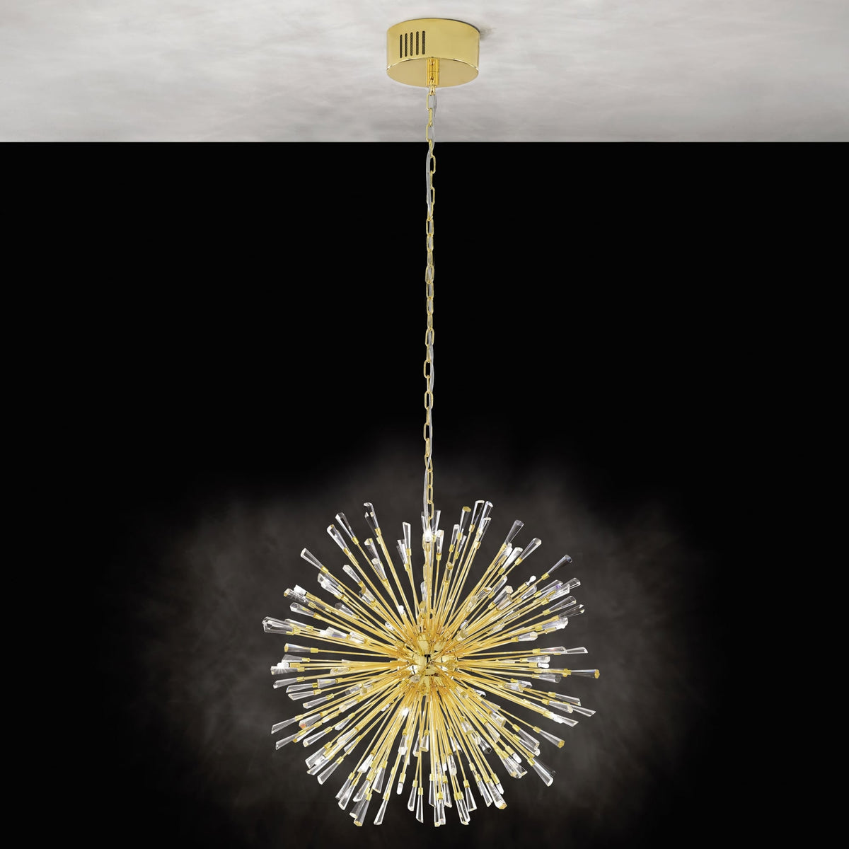 A gold pendant light with crystal rods hanging from a ceiling, against a black background.
