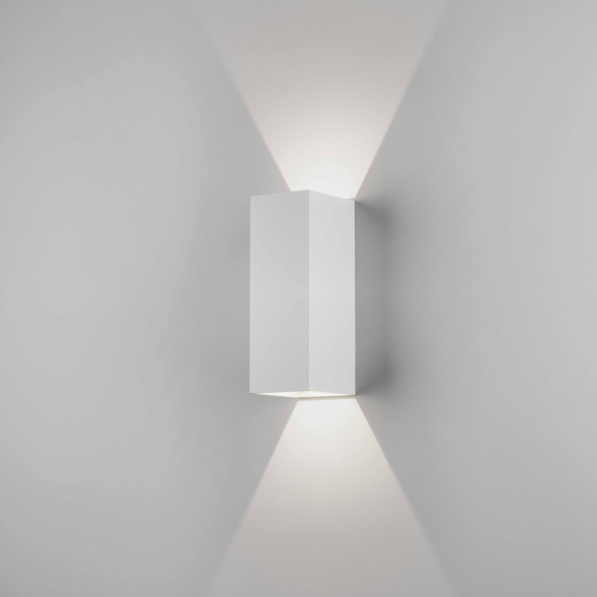 White rectangular wall light fixture casting light upwards and downwards on a light grey wall