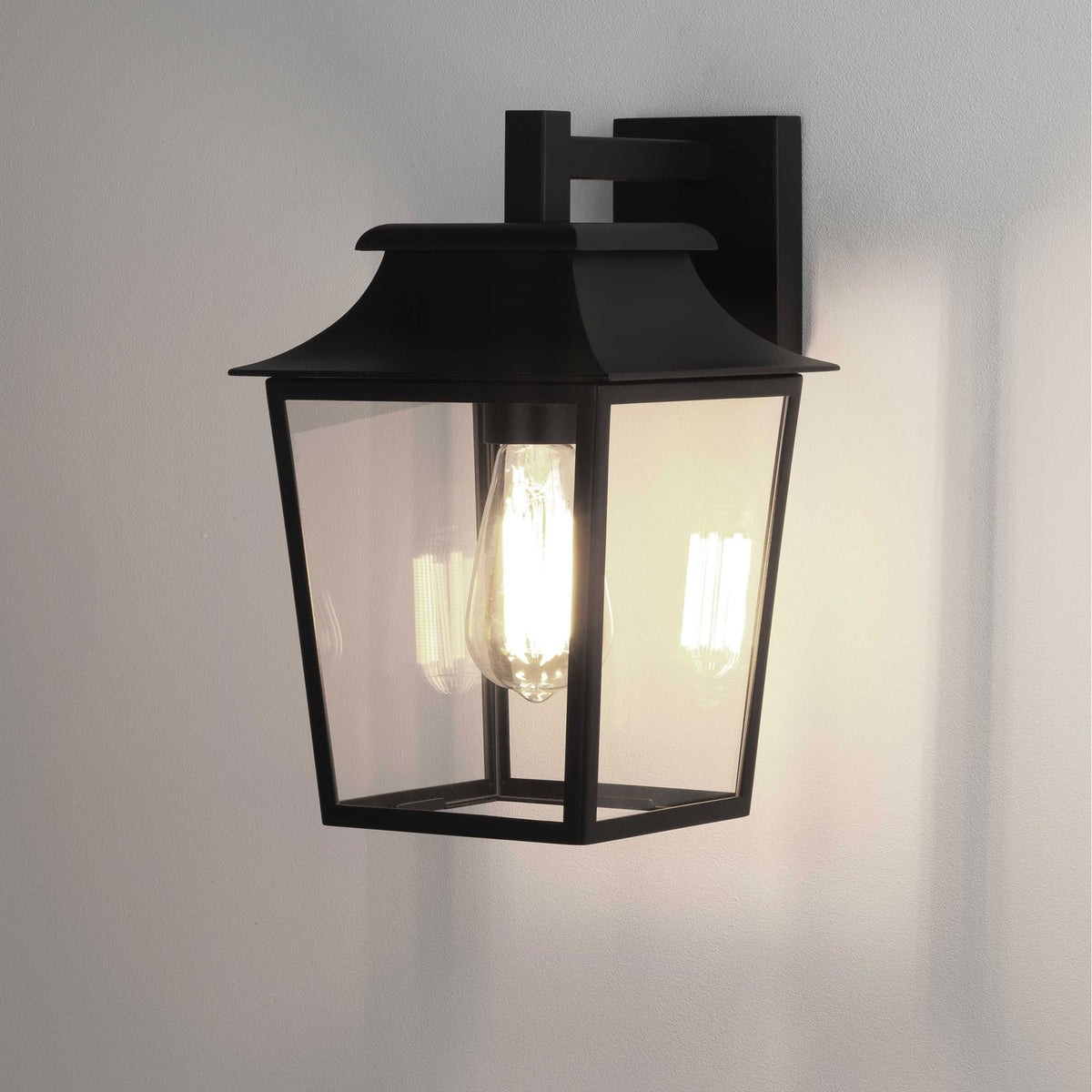Black outdoor wall light with clear glass panels and an exposed filament bulb