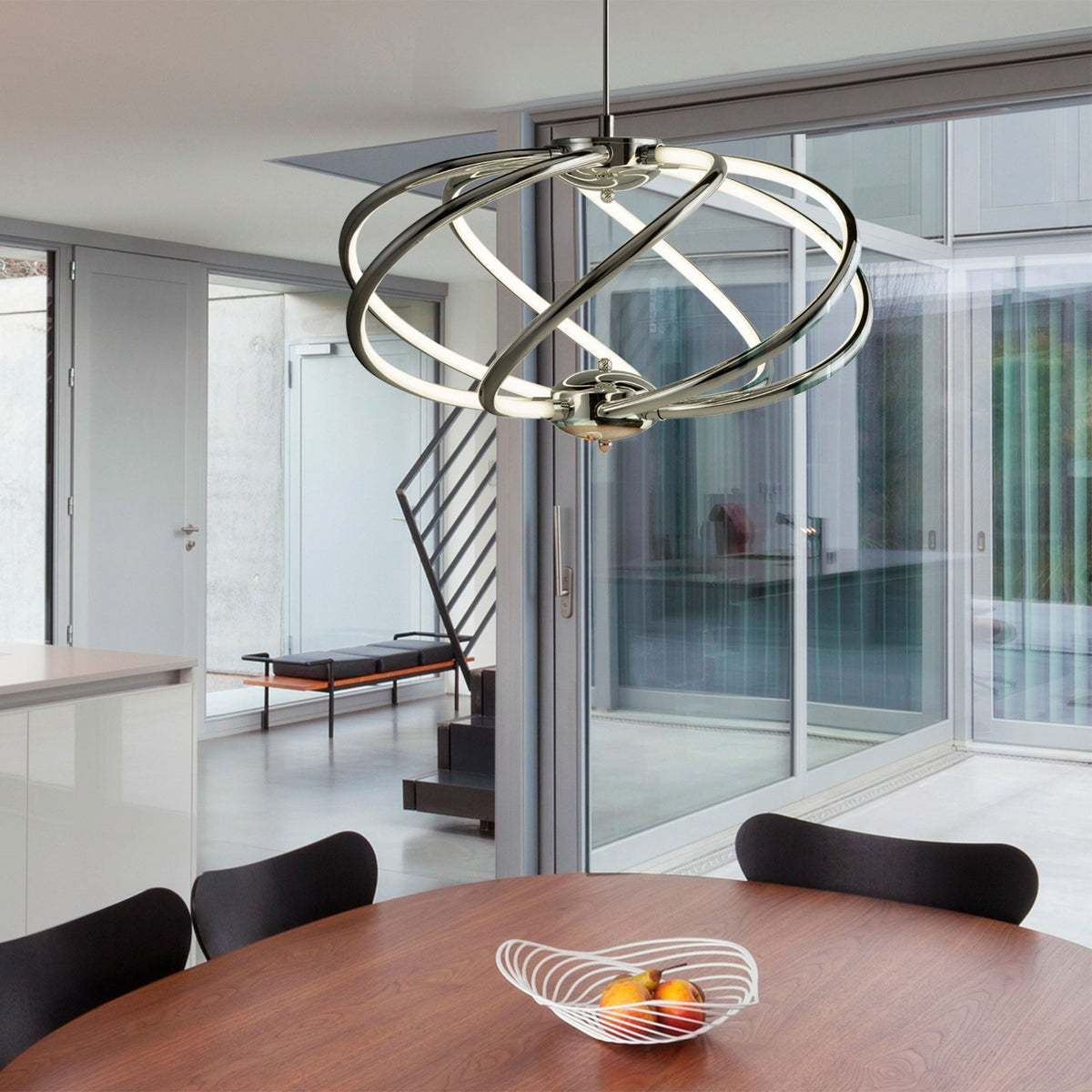 A modern chrome pendant light illuminates a dining area with a wooden table and black chairs.