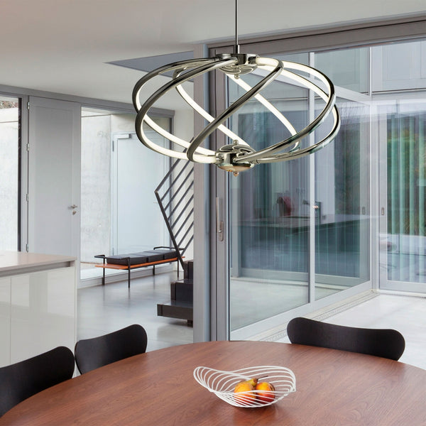 A modern chrome pendant light illuminates a dining area with a wooden table and black chairs.