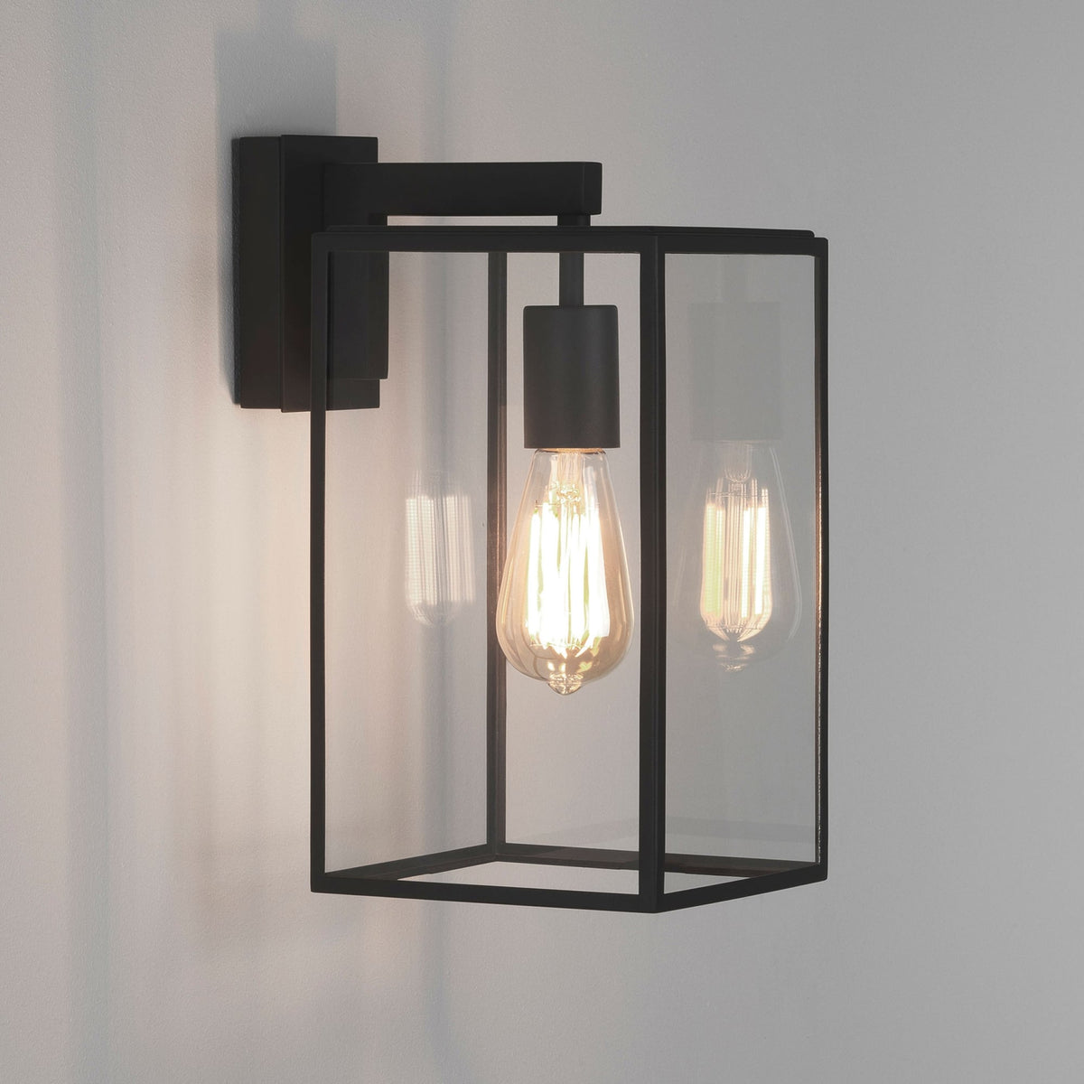 Black rectangular outdoor wall light with clear glass panels and an exposed filament bulb