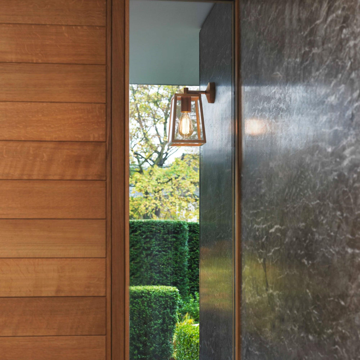 Outdoor wall light with a clear glass shade and exposed filament bulb, mounted on a grey marble wall