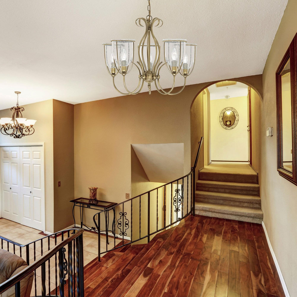 A contemporary chandelier illuminating a grand hall with wooden floors and a staircase.