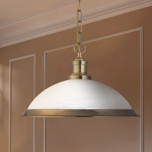 A close-up of a pendant light with a white dome shade and brass accents against a brown wall.