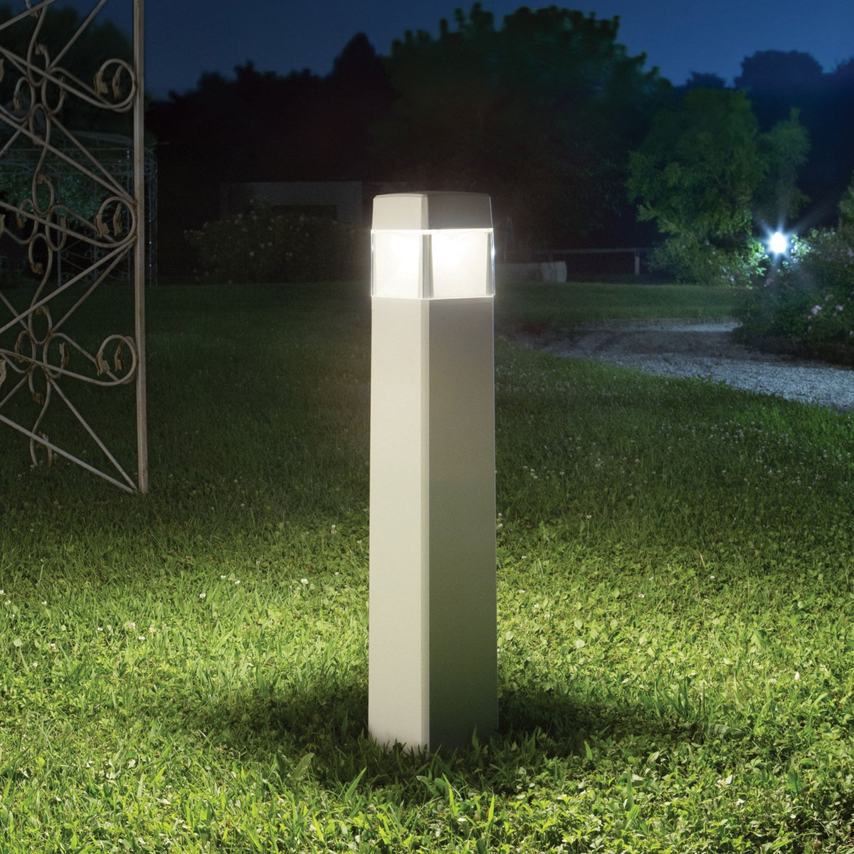 A modern outdoor bollard light illuminating a garden path at night.