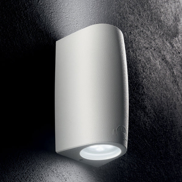 A white curved wall light with a downward-facing beam illuminates a textured dark wall.