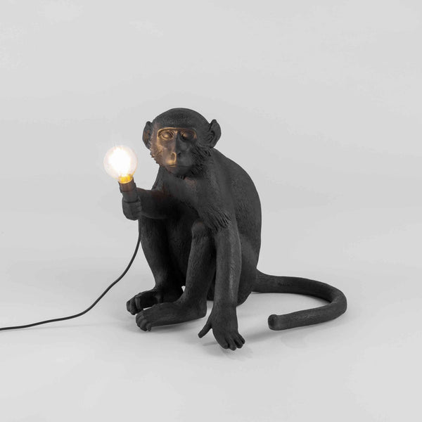 A black monkey table lamp with a glowing bulb. It adds a whimsical touch to any room.