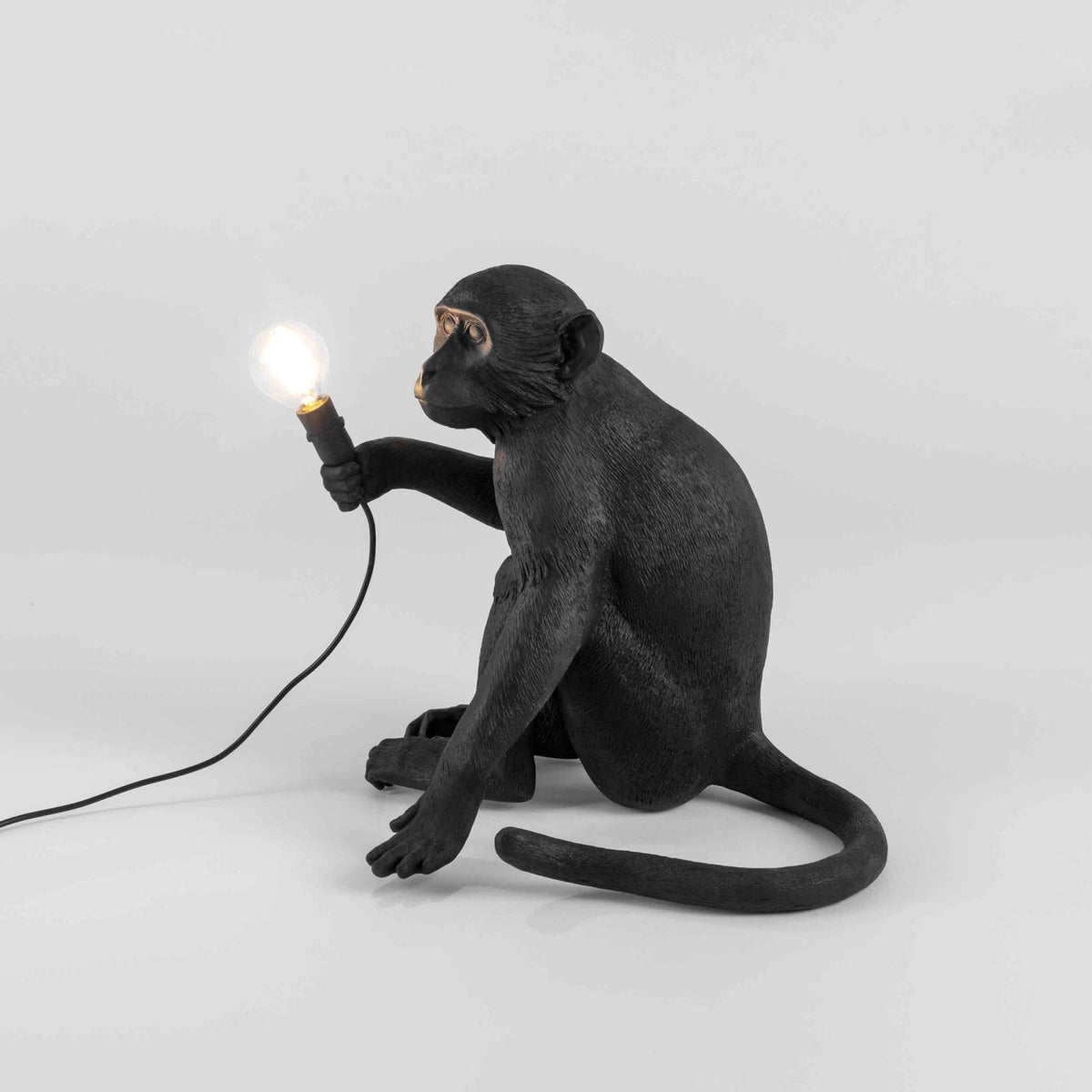 A black monkey table lamp with a glowing bulb viewed from the side, providing ambient light.