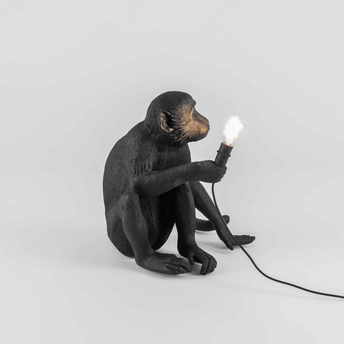 A black monkey table lamp with a glowing bulb, offering a playful and practical lighting solution.