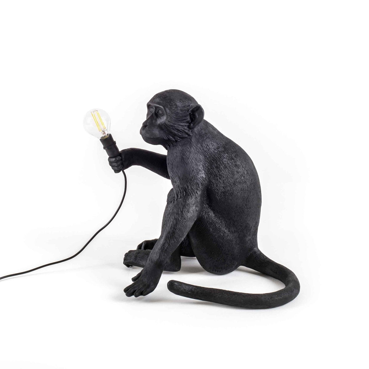 A black monkey table lamp holding a glowing bulb from a different angle, showcasing its design.